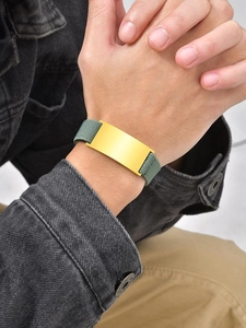 Wrist view of a gold curved plate bracelet with a sage green elastic braided band