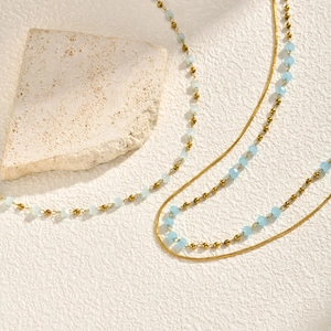 Detail view of gold layered necklace with light blue faceted beads on a textured surface