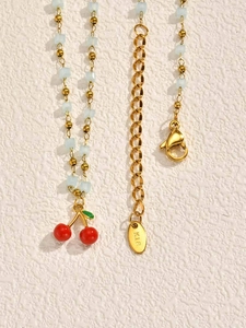 Detail of gold cherry pendant necklace with light blue beads and K18 hallmark clasp