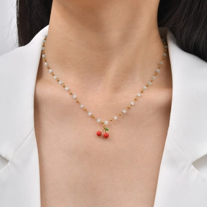 Detail of red cherry pendant necklace with light blue beads on a golden chain