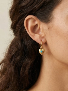 Close-up of heart-shaped gold earrings with turquoise stone worn by a model