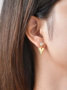 Macro shot of gold heart dangle earrings with zircons worn by a model in soft light