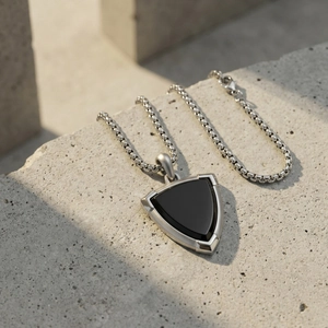 Stainless steel box chain necklace with black onyx shield pendant on concrete surface