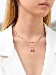 Close-up of layered gold chain necklace with light blue beads and a cherry pendant