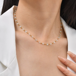 Detail of gold beaded necklace with light blue square sugar beads on a female model