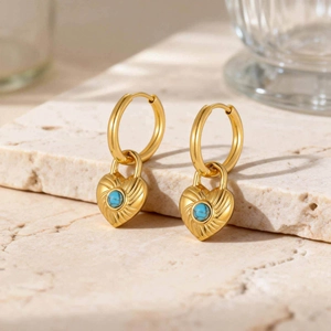 Golden heart lock earrings with turquoise inlay and sunburst texture on stone pedestal