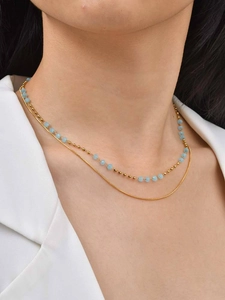 Close-up of double-layer gold necklace with blue beads and sleek snake chain style