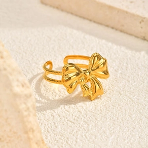 Detailed close-up of golden bow ring with beaded band on a textured stone surface