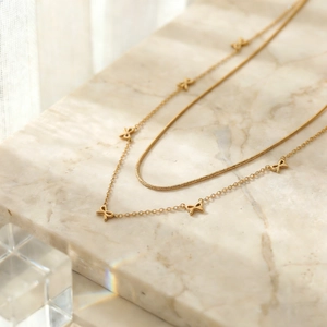 Détail du collier double rang doré avec pendentifs nœuds sur une surface en marbre élégante