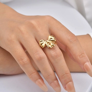 Detail of a polished golden bow knot ring with ribbon texture on a model hand