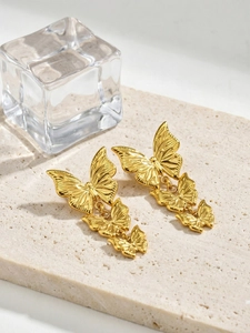 Detail of elegant gold triple butterfly drop earrings on a minimalist stone background
