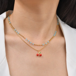 Double-layered gold beaded necklace with light blue spacers and a red cherry pendant