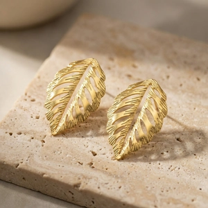 Golden hollow leaf stud earrings with brushed texture on natural stone surface