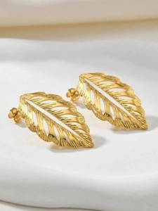Macro shot of gold hollow leaf earrings with brushed texture on white ceramic tray