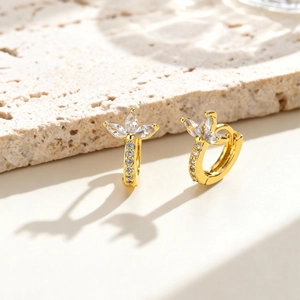 Luxurious 18K gold clover huggie earrings with marquise cubic zirconia on stone background