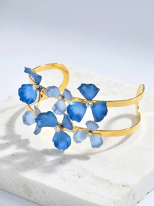 Detail of gold flower bangle with blue enamel petals and sparkling zircon on stone surface