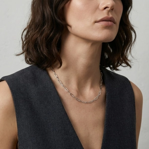 Detail of silver paperclip chain necklace on model wearing dark grey vest suit