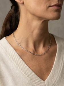 Detail of silver paperclip chain necklace styled on a white V-neck knitted sweater