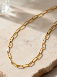 Minimalist gold paperclip chain necklace displayed on a textured stone pedestal base