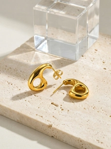 Vue détaillée des boucles d'oreilles dorées géométriques avec finition miroir sur fond pierre