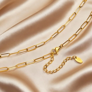 Macro detail of 18K gold-plated paperclip chain with lobster clasp on silk fabric
