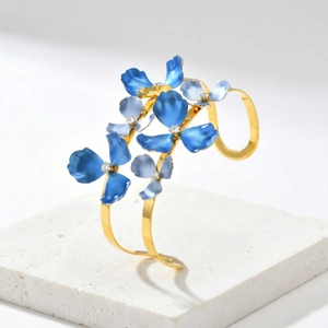 Elegant gold open bangle with blue enamel flowers and sparkling crystals on stone stand
