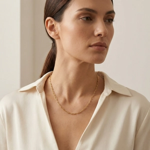 Close-up of a minimalist gold paperclip chain necklace worn with a silk V-neck shirt