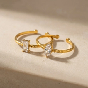 Golden open rings with marquise and emerald cut zircons on minimalist stone surface