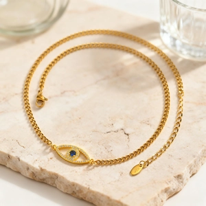 Goldene Evil Eye Kette mit blauem Stein auf Steinplatte, minimalistisches Edelstahl-Design