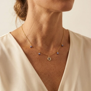 Gros plan du collier œil protecteur doré avec breloques en émail bleu sur un mannequin