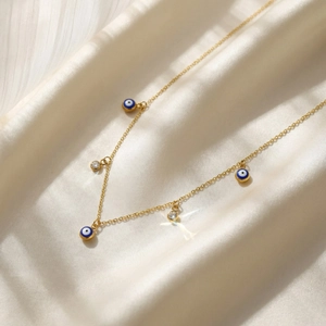 Détail macro d'un collier en chaîne dorée orné d'amulettes œil bleu et de cristaux étincelants chic