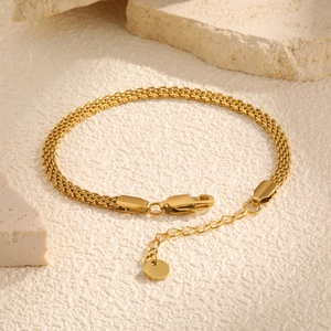 Macro view of gold mesh bracelet featuring woven texture with lobster clasp and charm