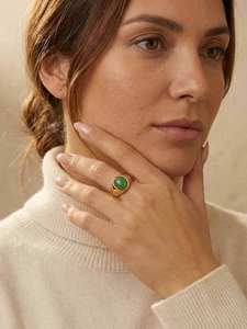 Gros plan d'une bague en acier doré sertie d'une pierre cabochon verte sur une main