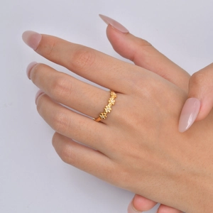 Detail of a gold flower ring with small zircons worn on finger against light background