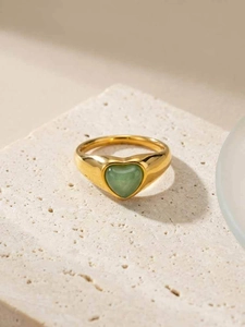 Gros plan d'une bague coeur dorée avec pierre aventurine verte sur plaque travertin