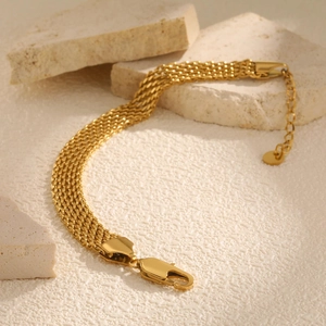 Close-up of golden multi-layer mesh chain bracelet with lobster clasp and round tag