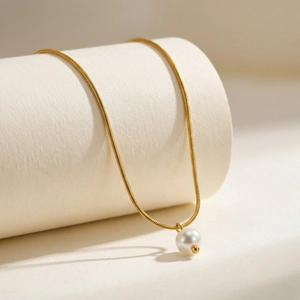 Collana a catena a serpente dorata minimalista con pendente a perla tonda su base bianca