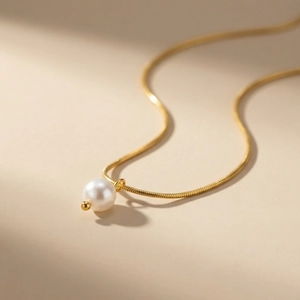 Collana minimalista a catena serpente dorata con ciondolo a perla bianca su sfondo caldo
