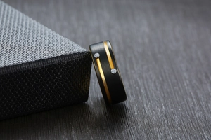 Macro shot of matte black tungsten ring featuring dual gold grooves and sparkling zircon inlay