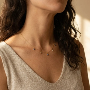Collier doré avec perles œil bleu et cristaux porté sur un pull en maille beige