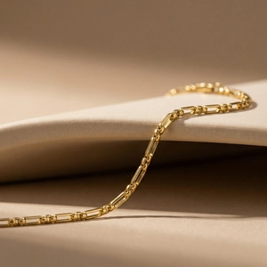 Detail of 18K gold plated Figaro pearl chain anklet on a minimalist beige background
