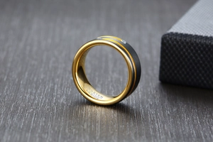 Detail of tungsten carbide ring with black matte finish and gold groove with two zircons