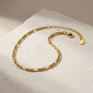 Detailed shot of golden Figaro anklet with lobster clasp on natural stone base