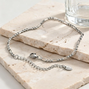 Macro detail of silver Figaro chain with lobster clasp and K18 hallmark tag on stone tray