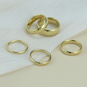 Set of five polished gold tungsten rings in varying widths displayed on silk fabric