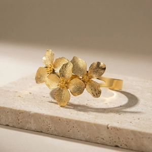 Bracelet jon jonc bohème doré avec fleurs brossées posé sur un support en pierre