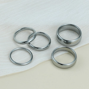 Macro detail of five dark grey tungsten wedding bands in various widths on white fabric