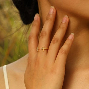 Close-up of golden cross ring with zircon inlay worn outdoors in soft sunlight