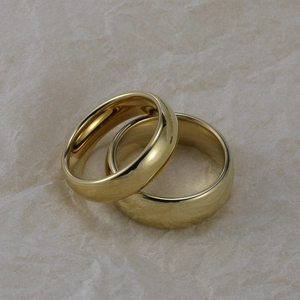 Close-up of a pair of polished gold tungsten rings on a textured cream background