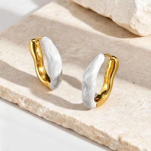 Détail de boucles d'oreilles vagues dorées et émail blanc sur pierre texturée